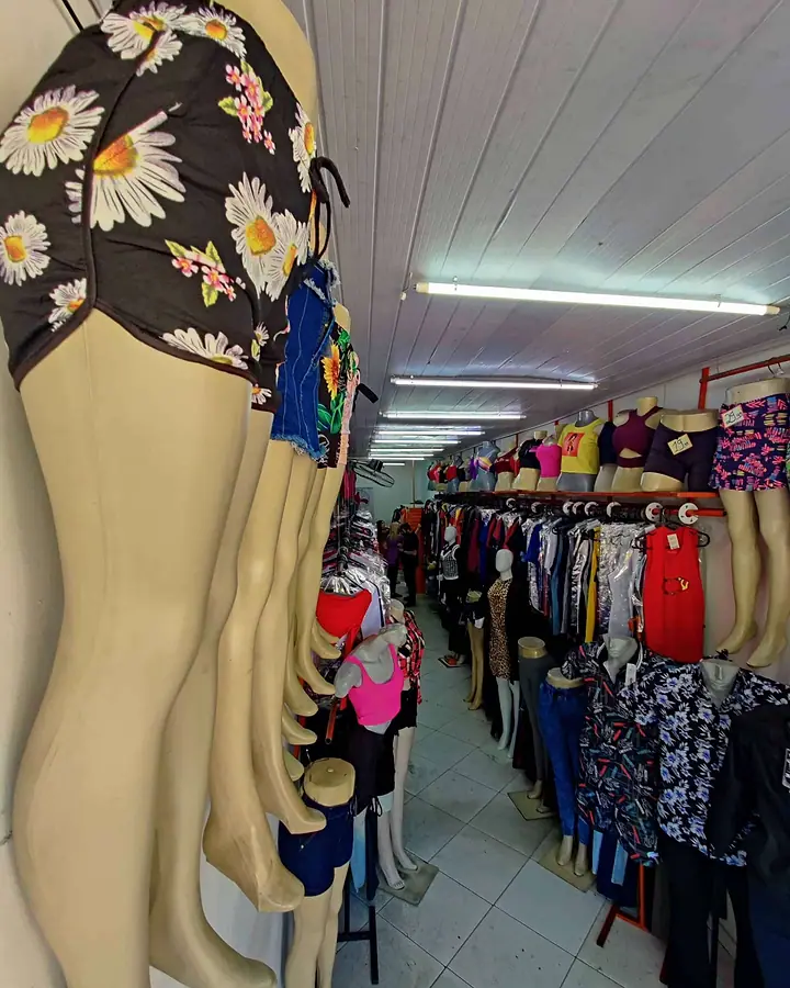 Corredor da loja com araras de roupas e manequins de calça