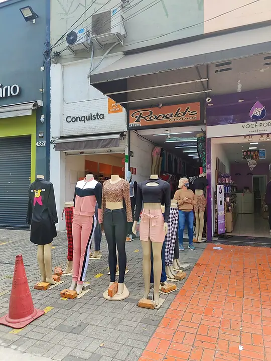 Fachada da Ronald's Fashion com o letreiro laranja e manequins vestidos na calçada