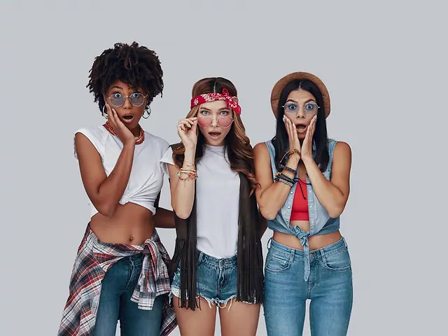 Três mulheres de calça jeans e camiseta, fazendo cara de surpresa
