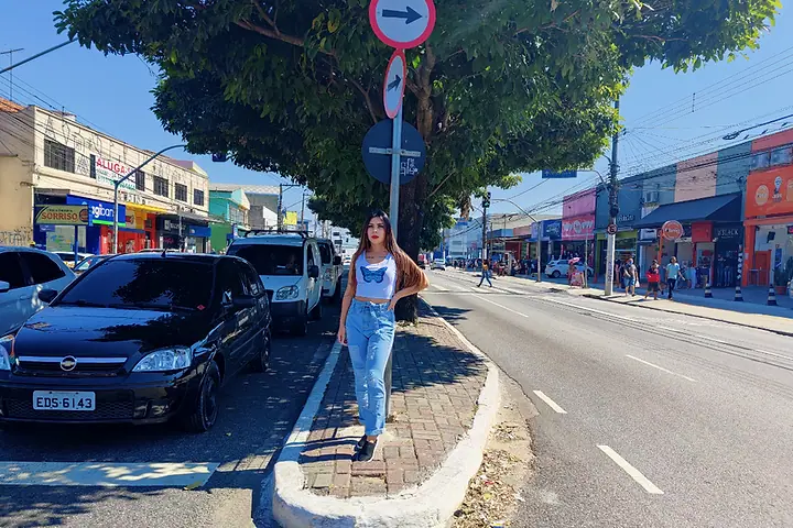 Mulher de calça jeans posando numa calçada arborizada do Itaim Paulista