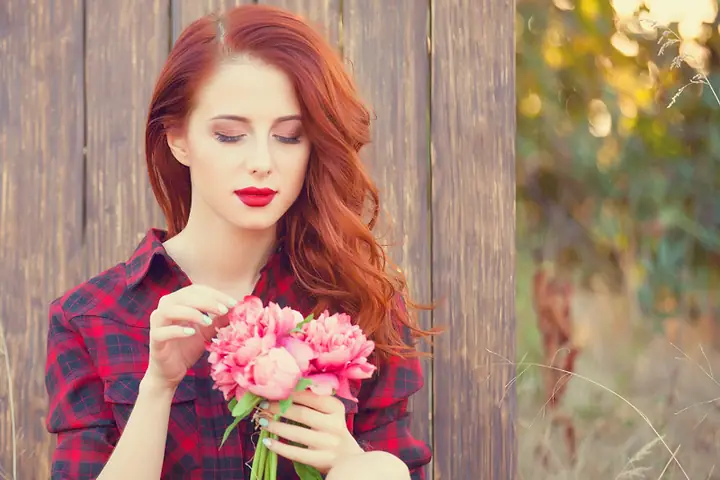 Mulher ruiva de camisa xadrez segurando um buquê de flores cor-de-rosa