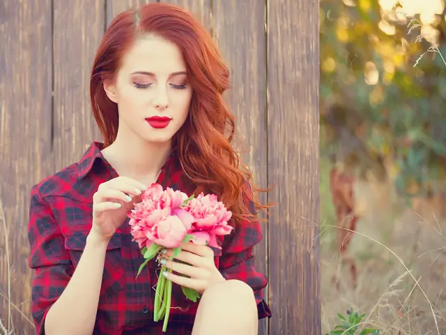Mulher ruiva de camisa xadrez segurando um buquê de flores cor-de-rosa